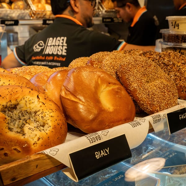 Freshly baked bagels and bialys displayed in a wooden basket at Bagel House, with staff in the background.