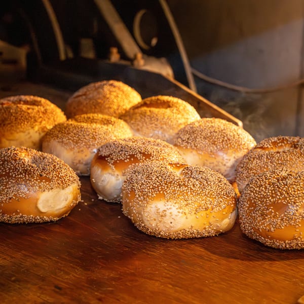 Freshly baked, golden-brown sesame bagels on a wooden surface, with steam rising from them.