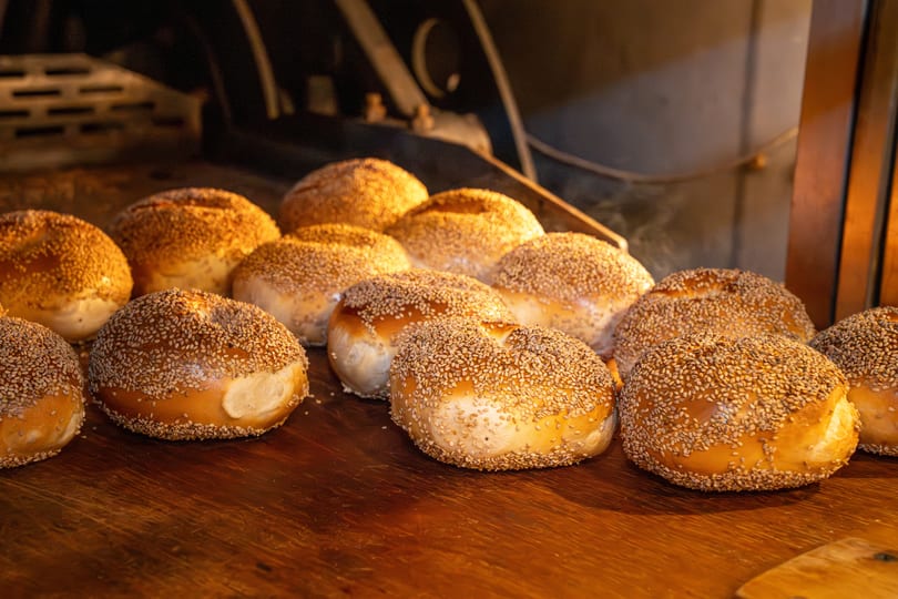 Freshly baked, golden-brown sesame bagels on a wooden surface, with steam rising from them.
