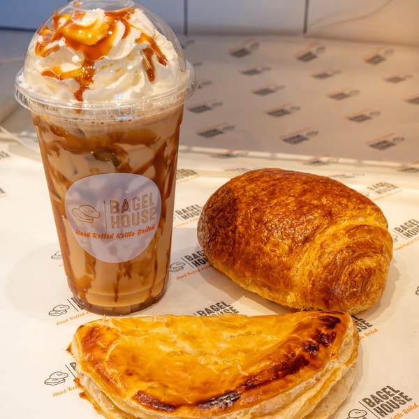 Iced coffee with whipped cream and caramel, a croissant, and a pastry on Bagel House branded paper.