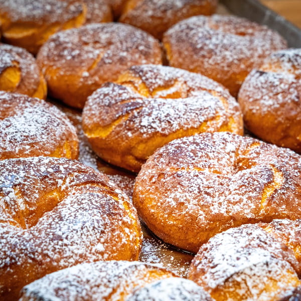 Close-up of many golden-brown, ring-shaped pastries dusted with powdered sugar on a tray.