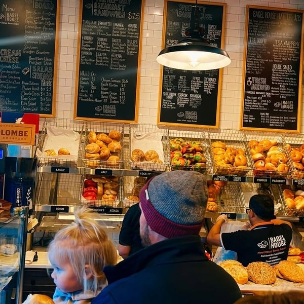 A bustling Bagel House interior with customers, staff, and shelves filled with various bagels and pastries.